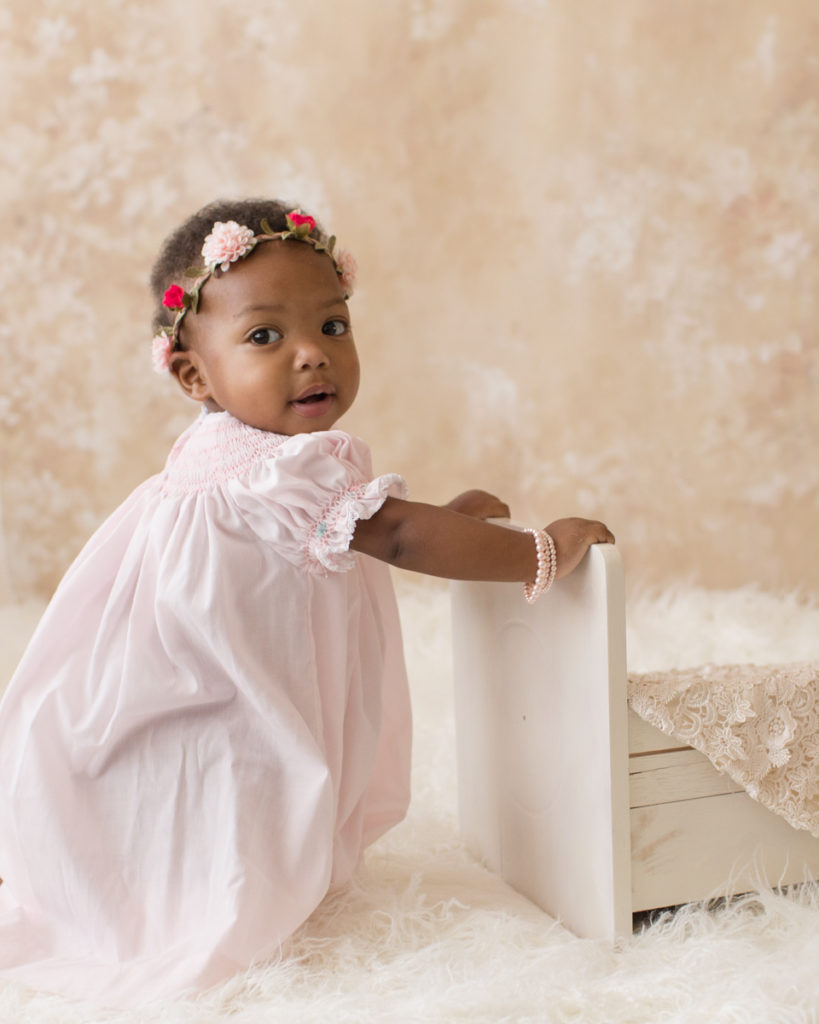 Rose One Year Old Baby Photos pulling up with pink smocked dress and floral crown pearls and ivory lace Gainesville Florida