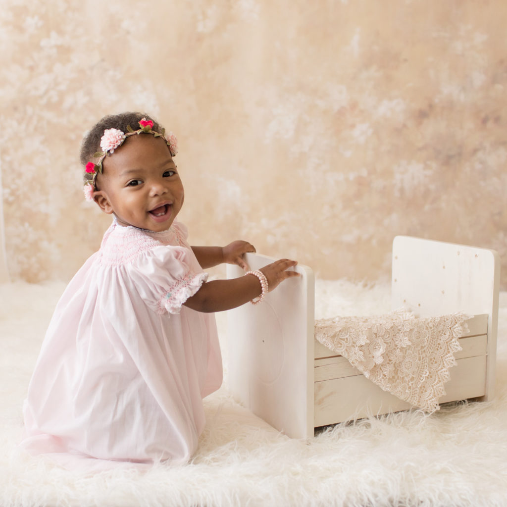 Rose One Year Old Baby Photos smiling with pink smocked dress and floral crown pearls and ivory lace pink and peach tones Gainesville Florida