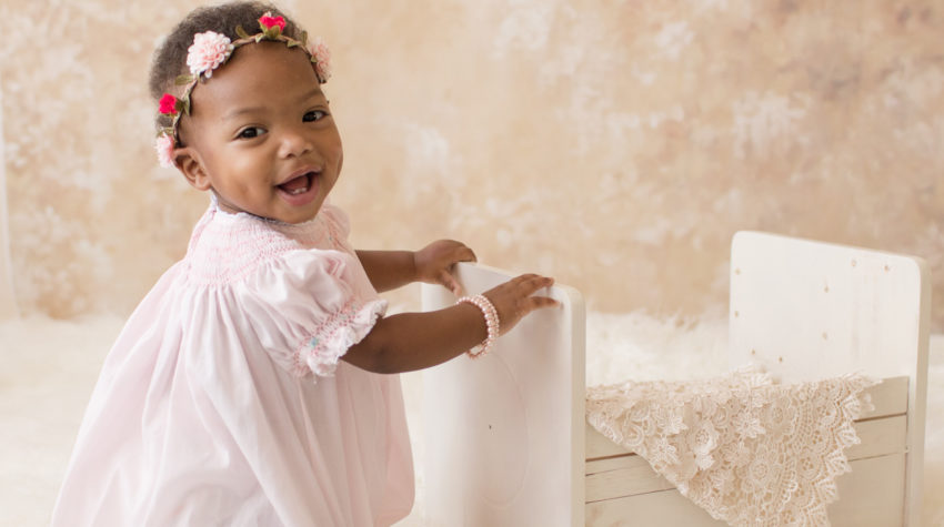 Rose One Year Old Baby Photos smiling with pink smocked dress and floral crown pearls and ivory lace pink and peach tones Gainesville Florida