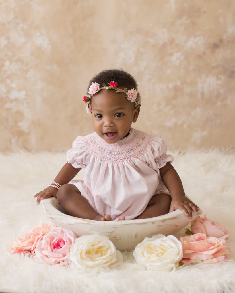 Rose One Year Old Baby Photos pink and peach tones sitting in white antiqued wooden bowl with pink smocked dress and floral crown pearls Gainesville Florida