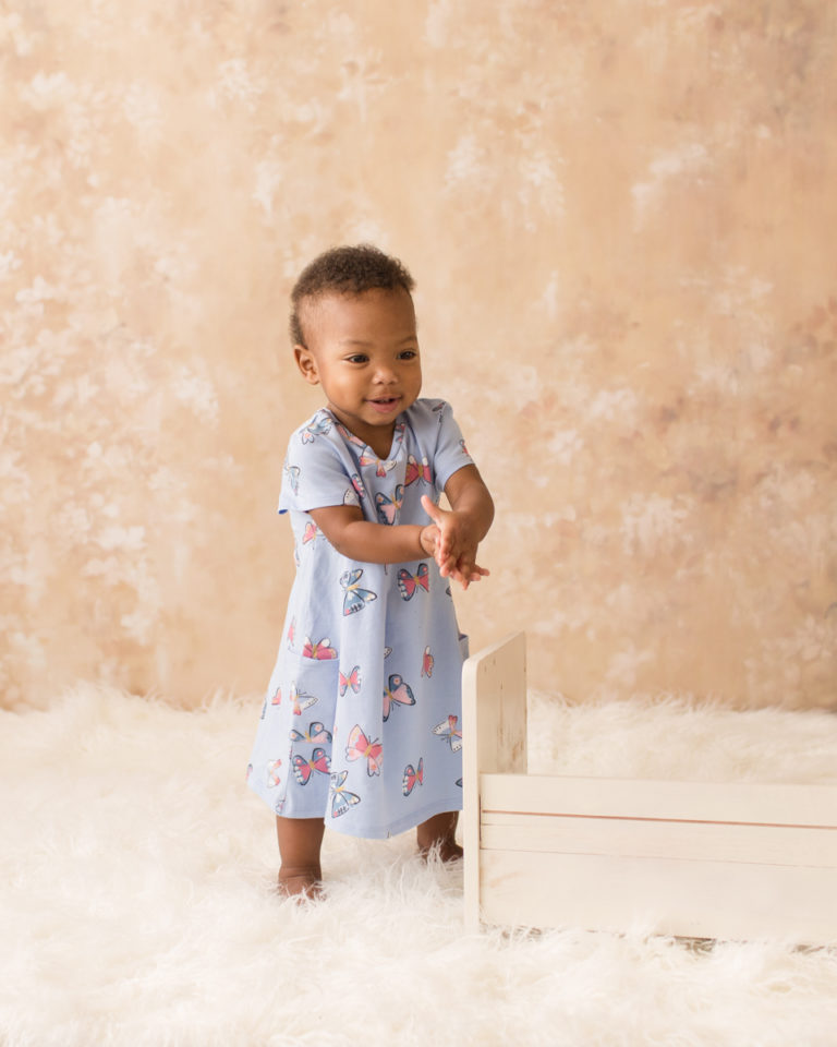 Rose One Year Old Baby Photos pink and peach tones clapping and standing alone with blue dress Gainesville Florida