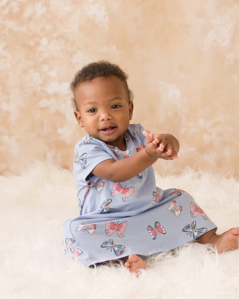 Rose One Year Old Baby Photos sitting and clapping with blue dress pink and peach tones Gainesville Florida