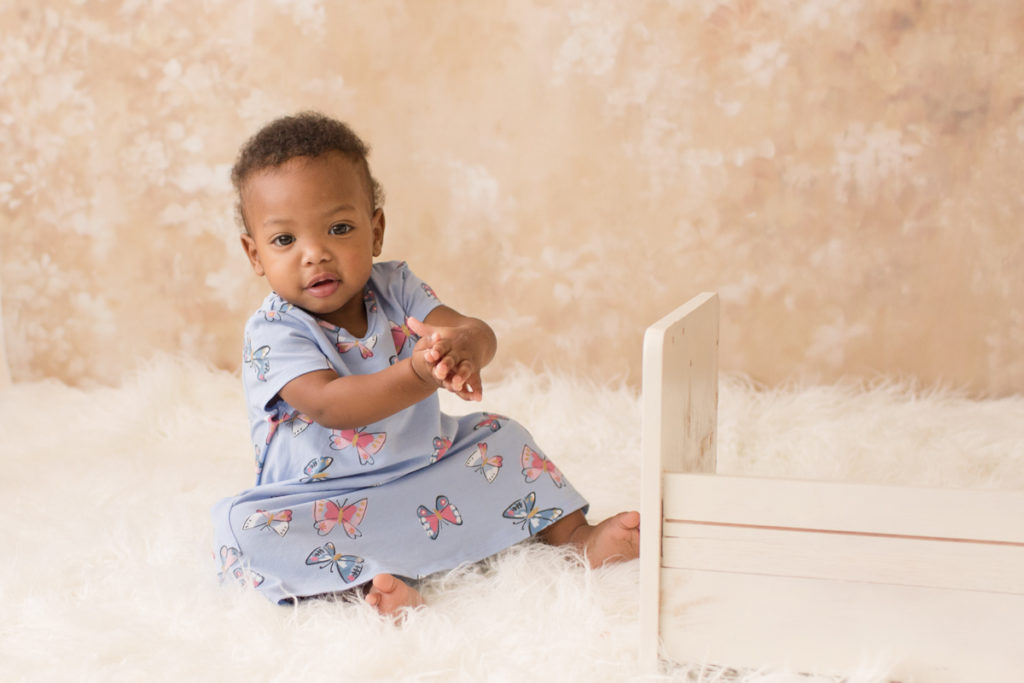 Rose One Year Old Baby Photos pink and peach tones sitting and clapping with blue dress Gainesville Florida