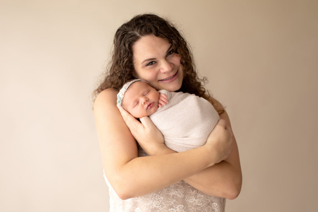 Hensley newborn photos teary eyed delighted Mom dressed in ivory lace holding tiny swaddled baby in beige wrap Gainesville Florida Newborn Photography