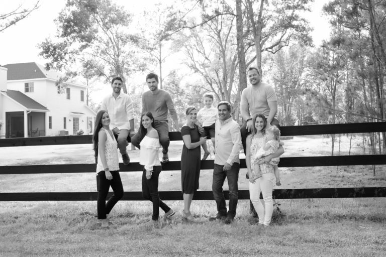 Three generations family with grandchildren posed at fence in light filled outside photo black and white Williston Florida