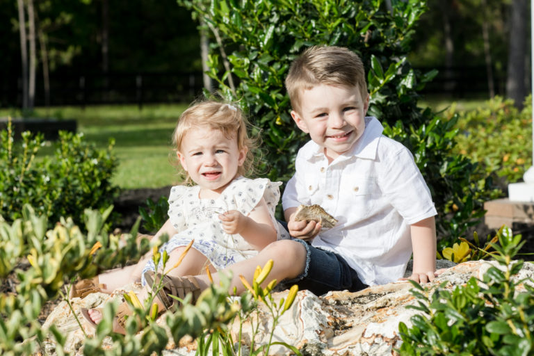 Toddlers dressed in white playing posed on large stone outside Williston Florida