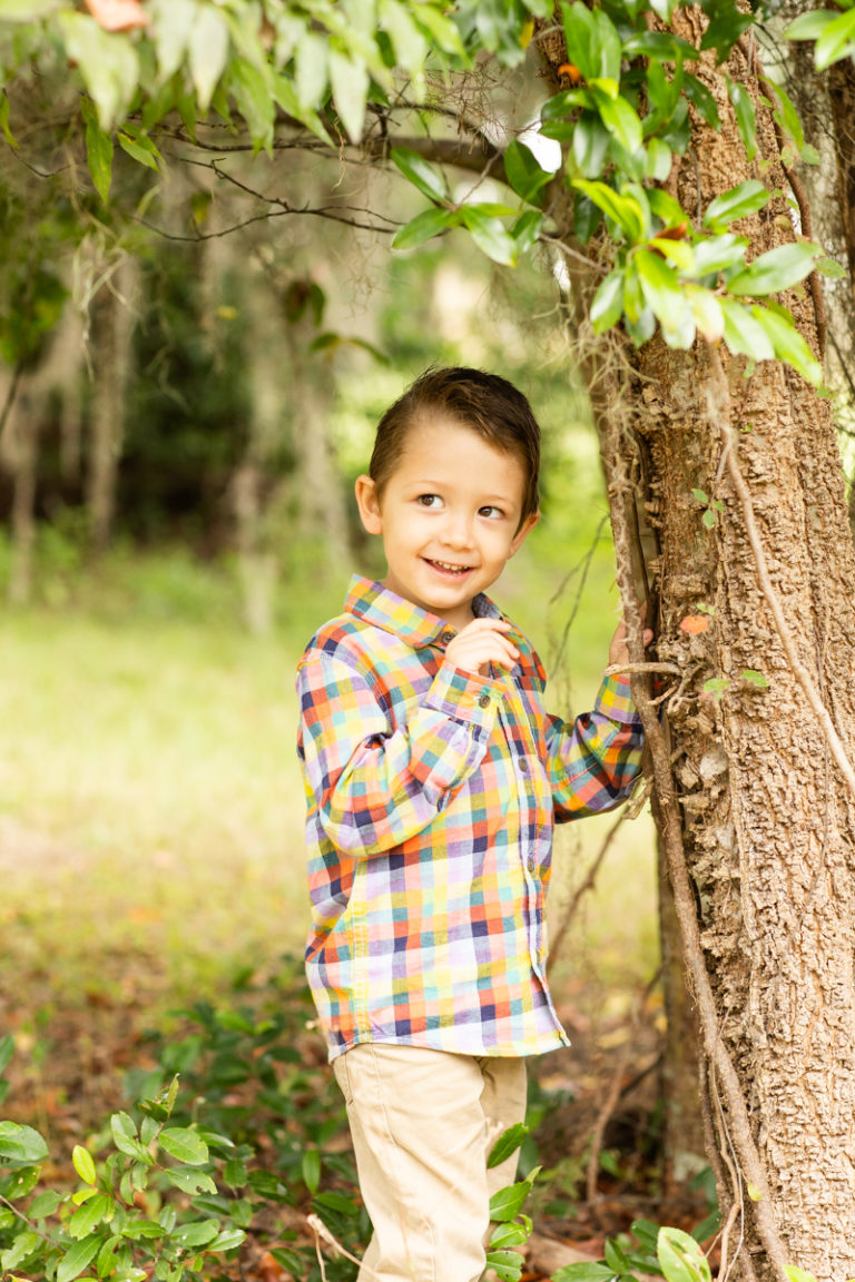 Three Year Old Boy with shy grin leaning against tree fall photos Horseshoe Farm Alachua Florida