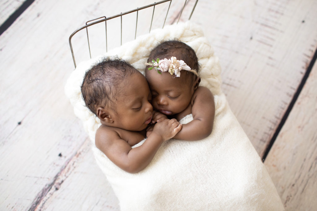 Twin Newborns Samuel and Sophia posed cuddling holding hands in metal newborn bed covered with cream blanket textured pillow distressed white floor in Gainesville Florida newborn photos taken angled from above