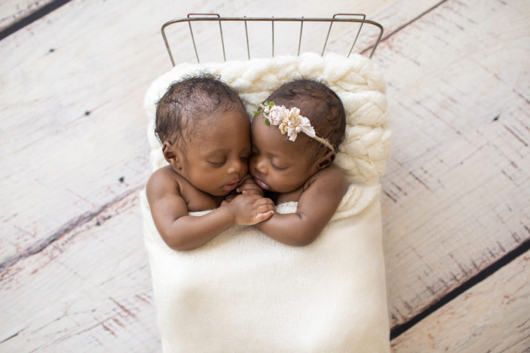 Twin Newborns Samuel and Sophia posed cuddling holding hands in metal newborn bed covered with cream blanket textured pillow distressed white floor in Gainesville Florida newborn photos taken from above