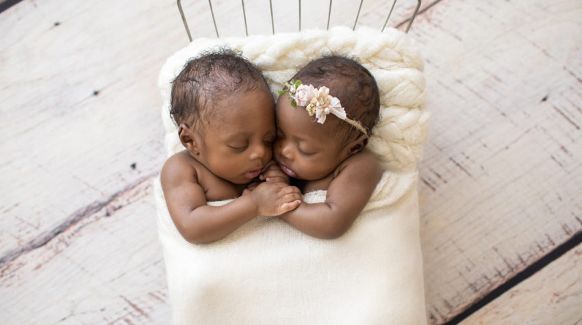 Twin Newborns Samuel and Sophia posed cuddling holding hands in metal newborn bed covered with cream blanket textured pillow distressed white floor in Gainesville Florida newborn photos taken from above