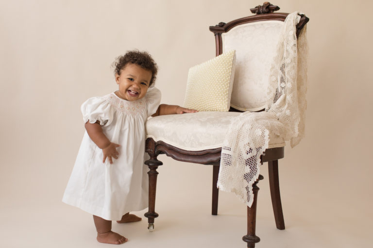 One year old Sara standing at ivory victorian chair with lace smocked white dress milestone session Gainesville Florida