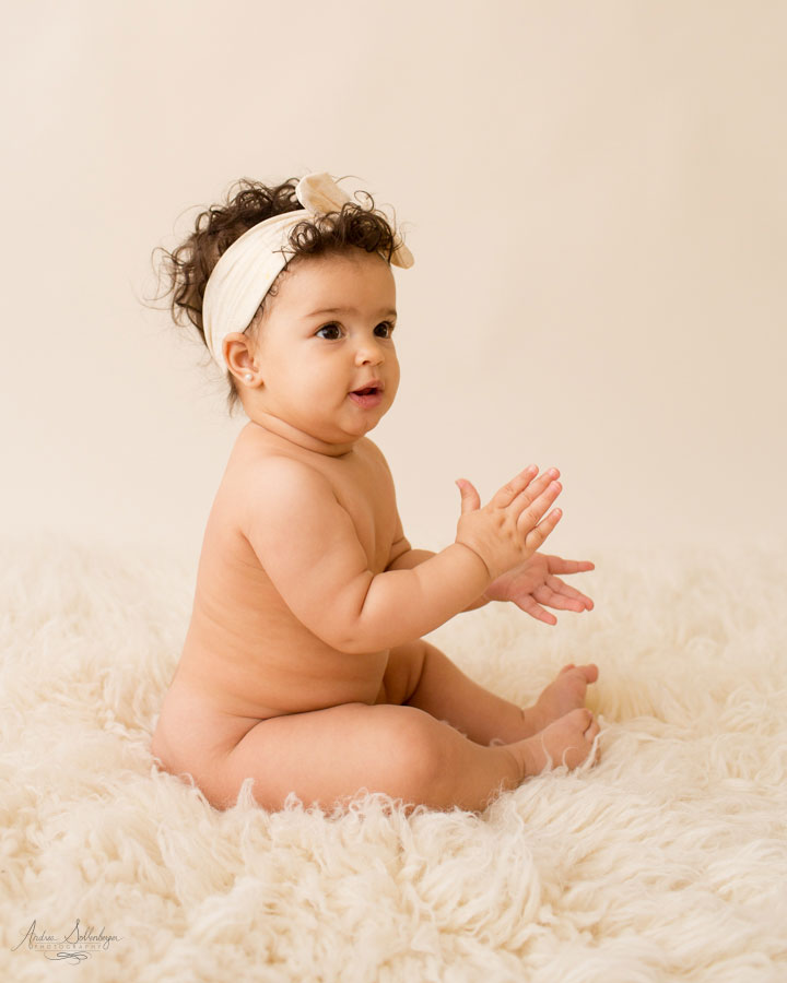 Baby rolls and clapping hands nine month naked baby on white.