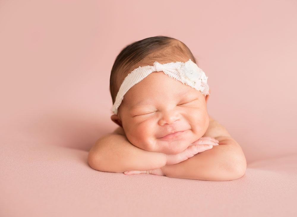 Baby girl grins propped up on arms in Newborn Photo session on Soft Pink Baby Blanket Gainesville FLorida