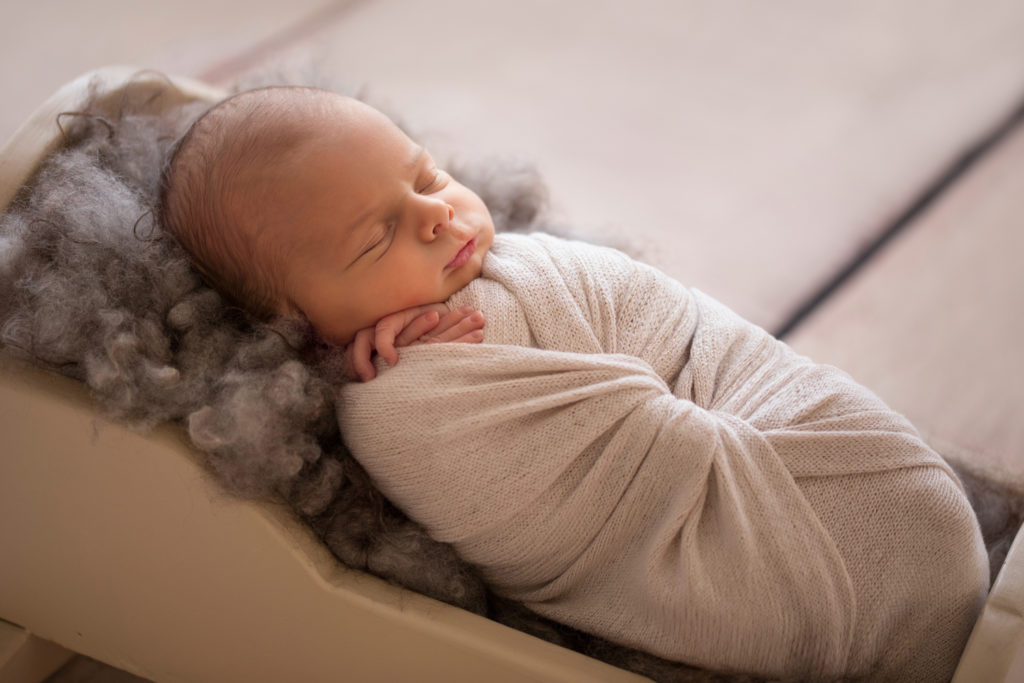 Newborn baby boy Nathan in cream wrap posed on brown wool in a cradle newborn portrait with backlight