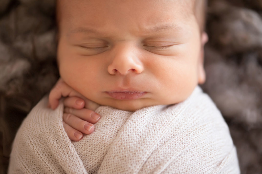 Newborn baby boy Nathan close up in cream wrap posed on brown wool in a cradle newborn portrait