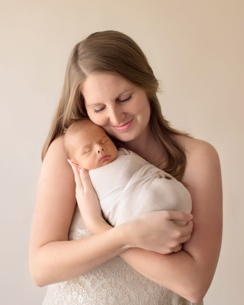 Beautiful mom tenderly cuddling newborn boy wrapped in cream soft neutral colors mom gazing at baby Gainesville FL newborn photography