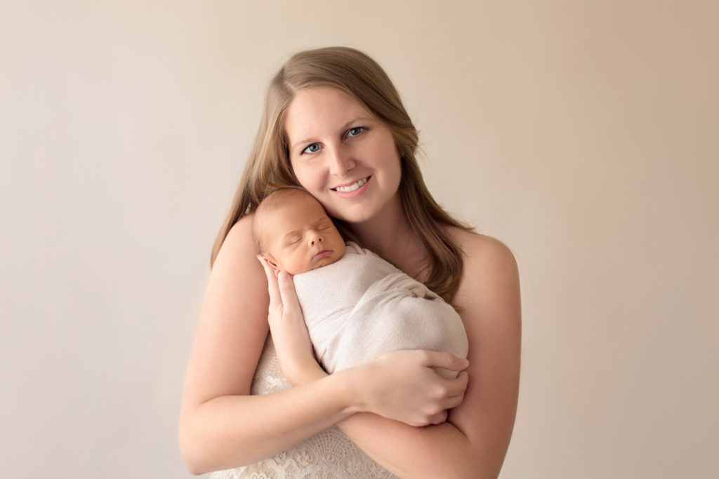 Beautiful mom tenderly cuddling newborn boy wrapped in cream soft neutral colors mom smiling at camera Gainesville FL newborn photography