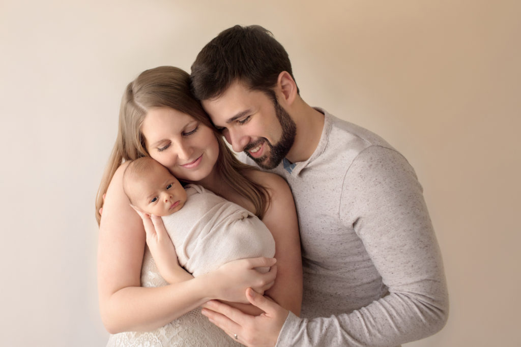 Newborn wrapped baby with tender mom and dad cuddle first family portrait soft neutral colors looking at baby Gainesville FL newborn photography