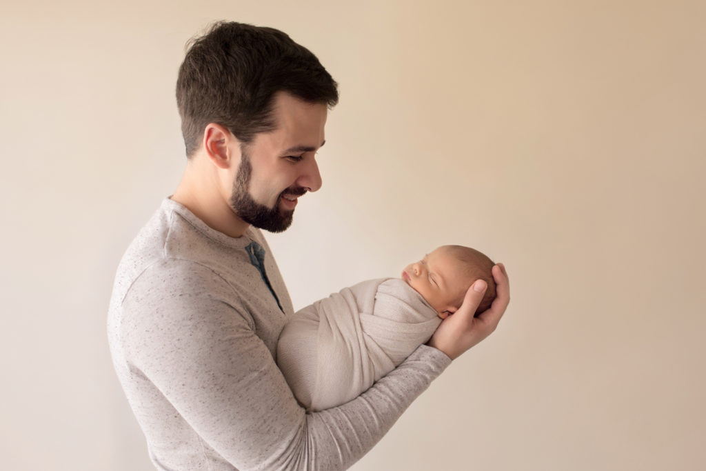 Handsome dad tenderly gazing at newborn boy wrapped in cream soft neutral colors profile photo Gainesville FL newborn photography