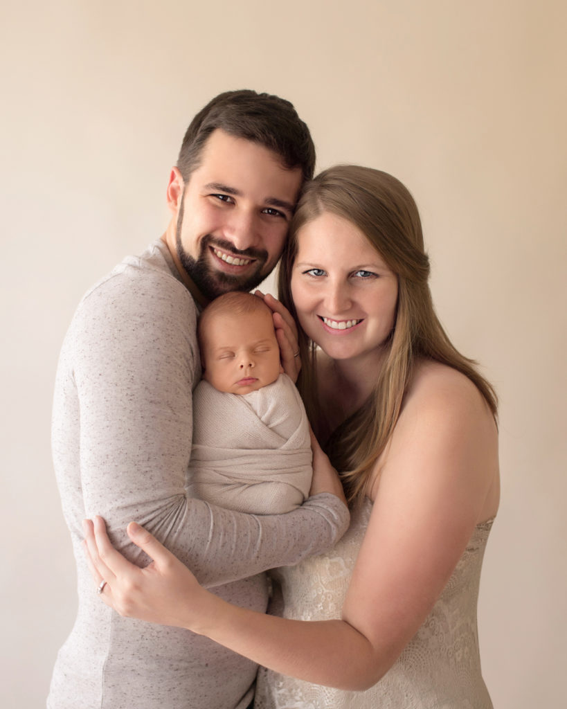 Newborn wrapped baby with tender mom and dad cuddle first family portrait soft neutral colors smiling at camera Gainesville FL newborn photography