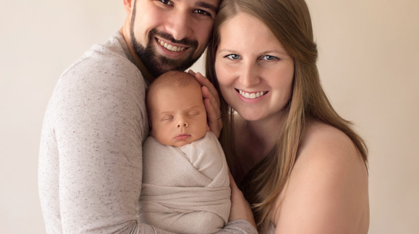 Newborn wrapped baby with tender mom and dad cuddle first family portrait soft neutral colors smiling at camera Gainesville FL newborn photography