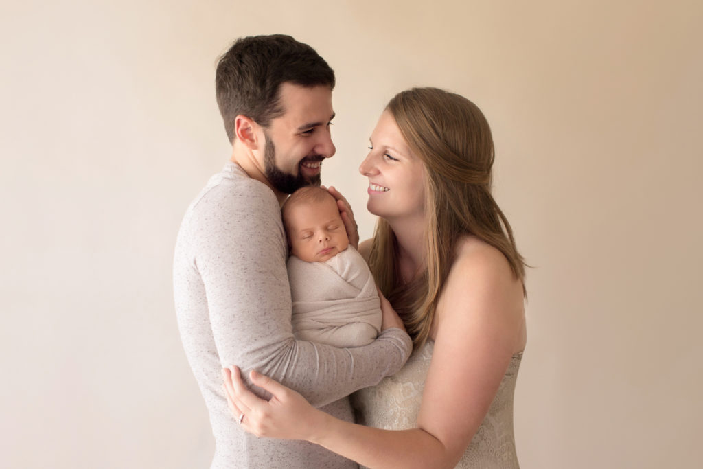 Newborn wrapped baby with tender mom and dad cuddle first family portrait neutral colors smiling at each other Gainesville FL newborn photography