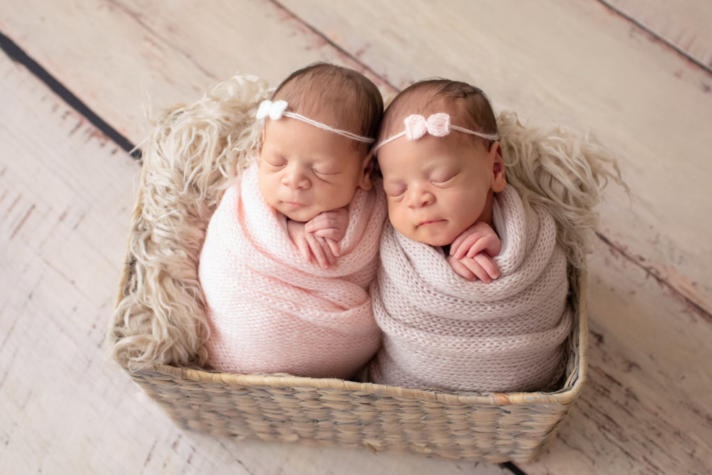 Newborn Twin girl photos baby smile Janae and Renae in pink handmade knit wraps and tiny knit bow head ties in a fur stuffed basket