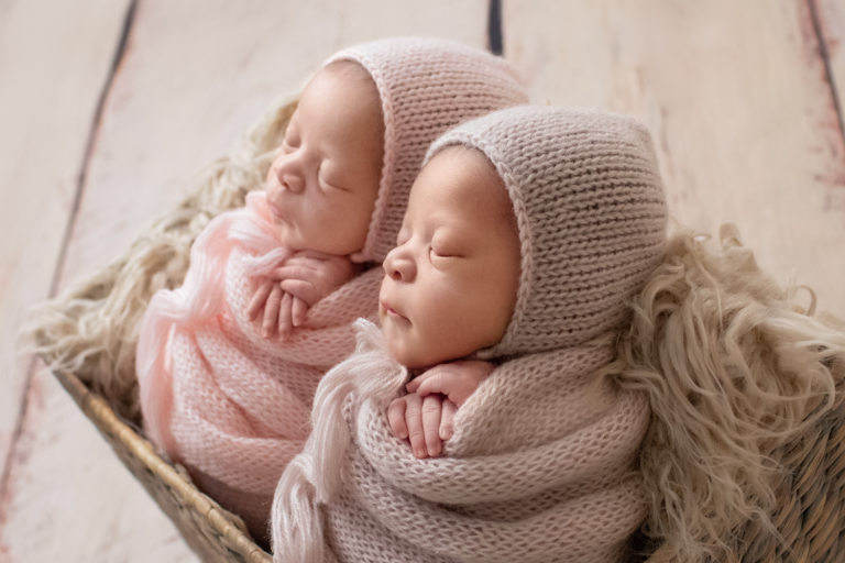 Newborn Twin girl photos Janae and Renae in pink handmade knit wraps and bonnets in a fur stuffed basket backlight