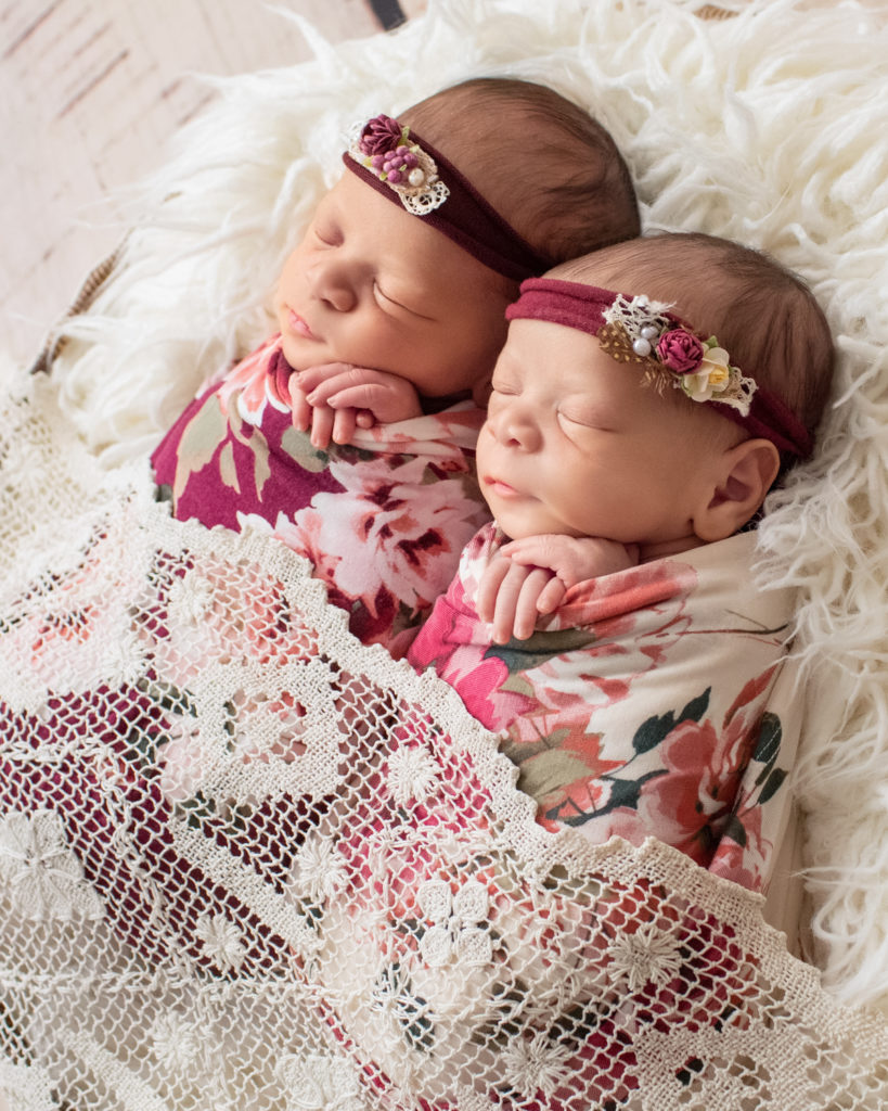 Newborn twin girls photos Renae and Janae in rose and burgundy floral wraps and floral head ties in a fur stuffed round basket draped in lace