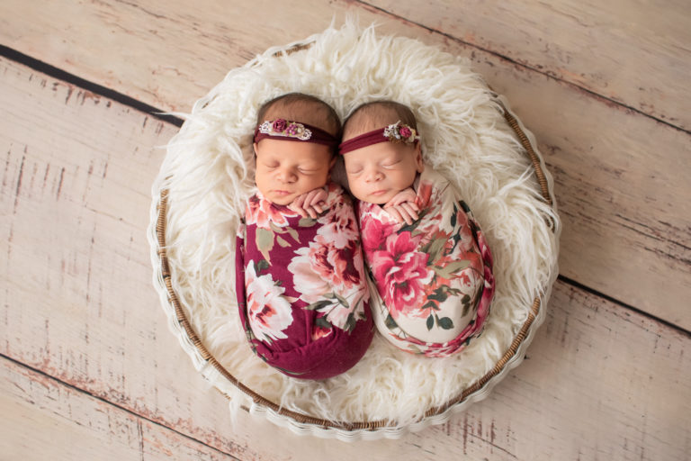 Newborn twin girls photos Renae and Janae in rose and burgundy floral wraps and floral head ties in a fur stuffed round basket