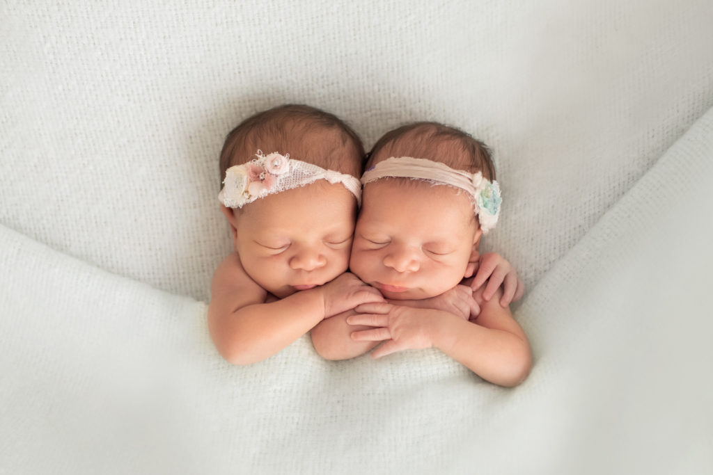 Newborn twin girls photos Janae and Renae tucked into mint green blanket hugging each other wearing floral headties