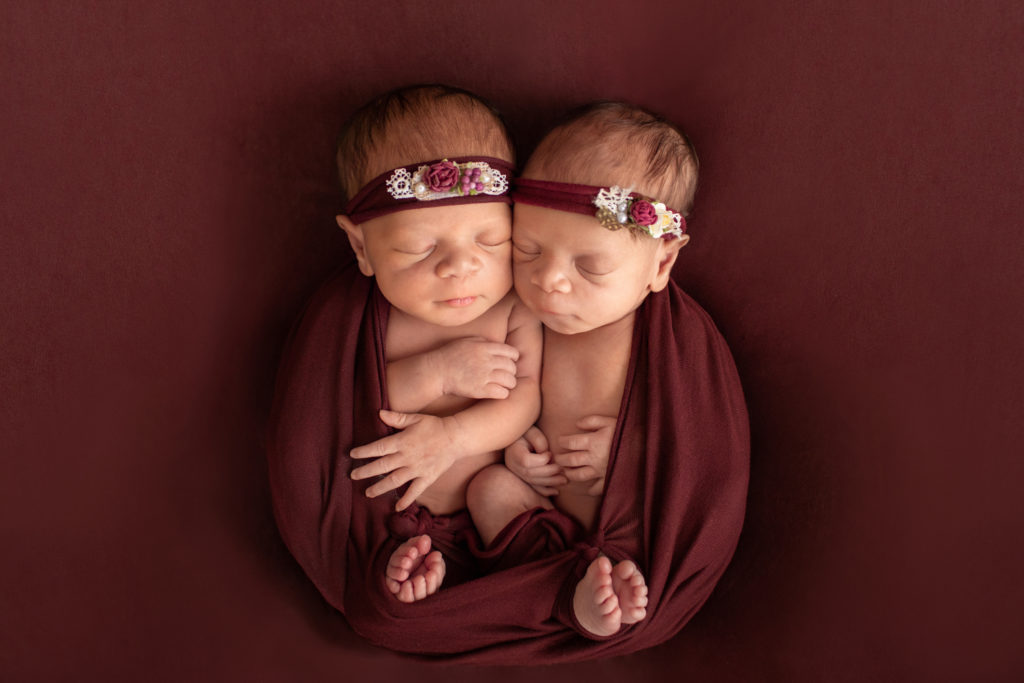 Newborn twin girls photos Janae and Renae toes together in burgundy wrap and floral head ties