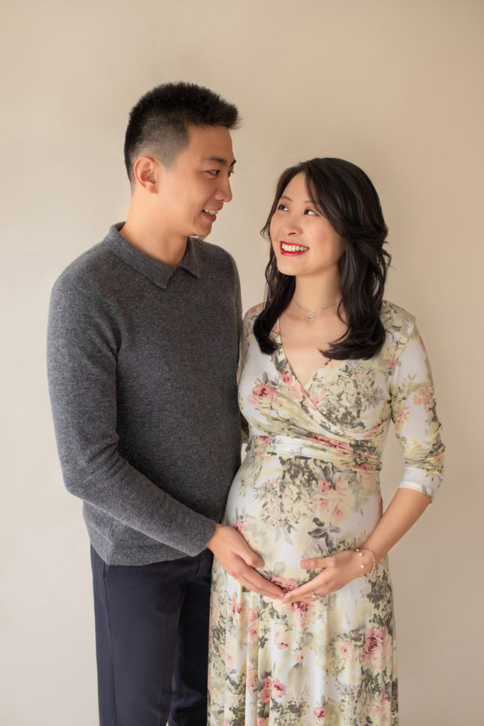 Maternity photos mom wearing floral pink and sage maternity gown in an ivory jersey fabric profile shot mom and dad smiling at each other