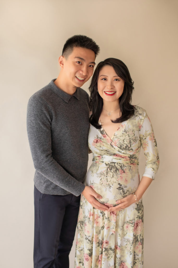 Maternity photos mom wearing floral pink and sage maternity gown in an ivory jersey fabric profile shot mom and dad smiling at camera