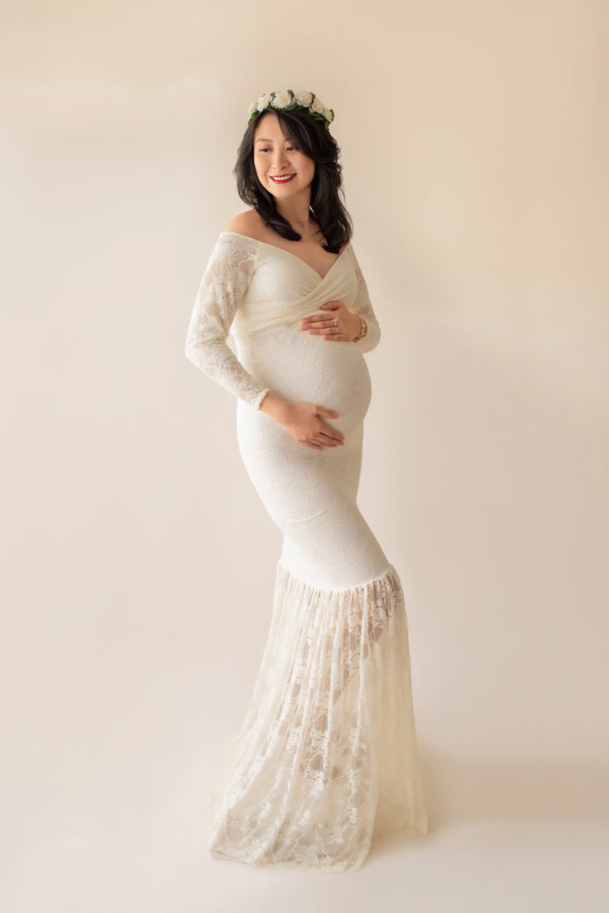 Maternity photo pregnant mom in elegant ivory lace long sleeve fitted gown with circular train wearing ivory floral crown smiling across her shoulder full shot to floor Gainesville Florida Maternity Photographer