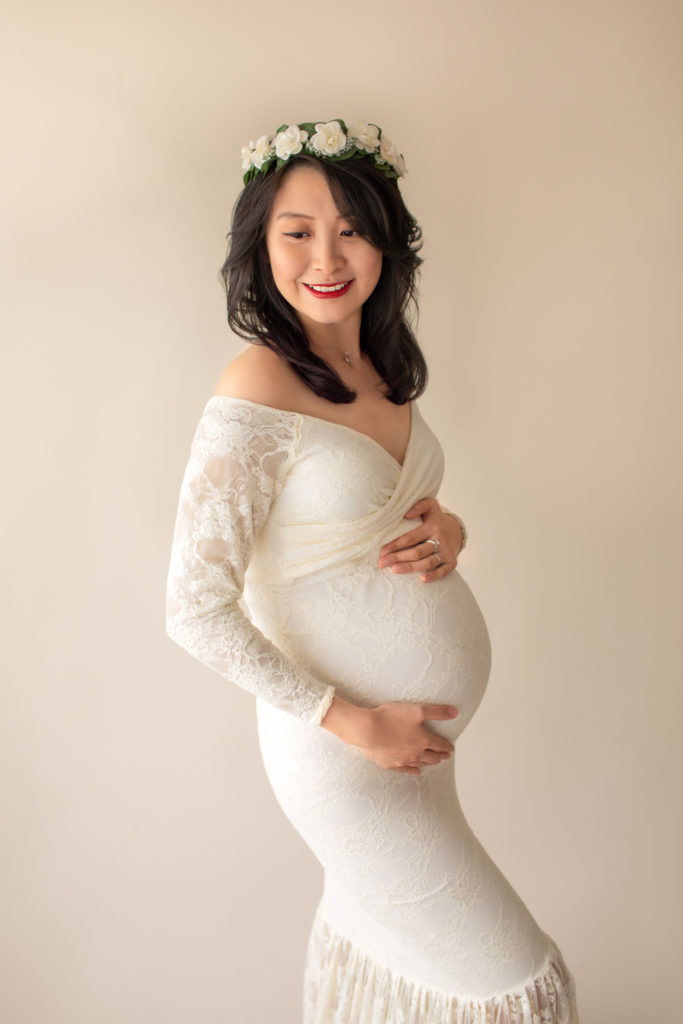 Maternity photo pregnant mom in elegant ivory lace long sleeve fitted gown with circular train wearing ivory floral crown looking toward her shoulder close up Gainesville Florida Maternity Photographer