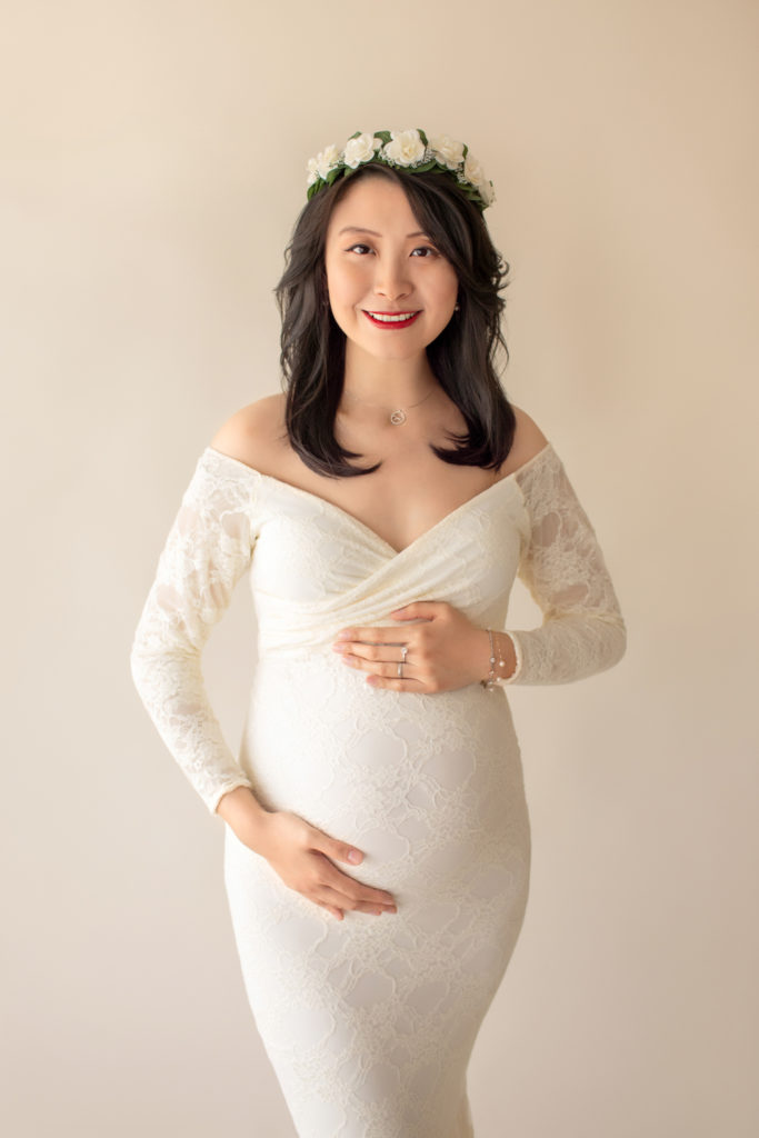 Maternity photo pregnant mom in elegant ivory long sleeve lace fitted gown with circular train wearing ivory crown smiling at camera Gainesville Florida Maternity Photographer
