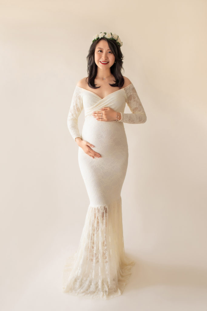 Maternity photo pregnant mom in elegant ivory lace long sleeve fitted gown with circular train wearing ivory floral crown smiling at camera full shot to floor Gainesville Florida