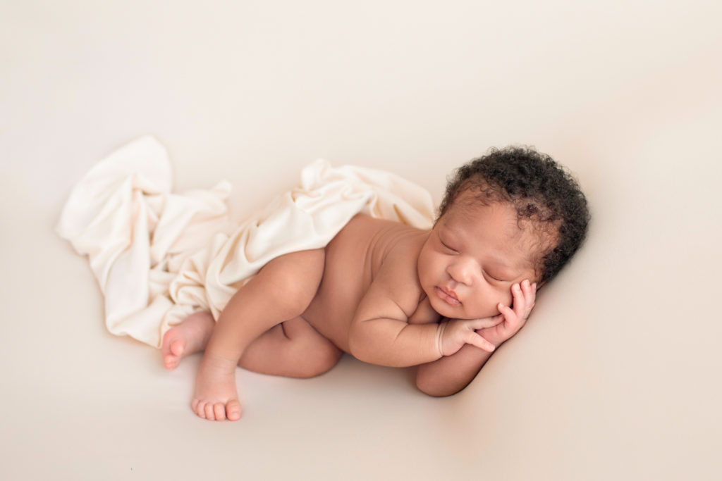 Gainesville newborn photos naked little baby hands curled around his round cheeks so close to his face posed on his side head full of curly brown hair