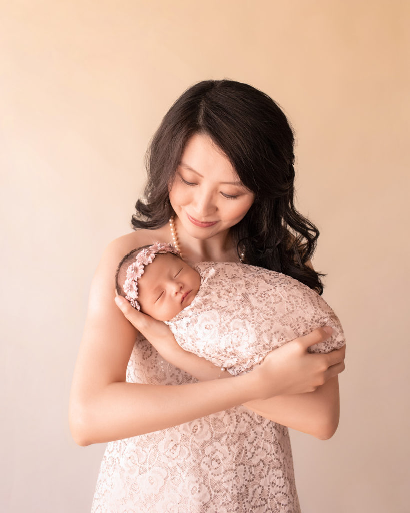 Gainesville newborn portraits beautiful mom Vera holding close her baby girl wrapped in matching cream fabric with sequins and wearing floral dusty pink crown