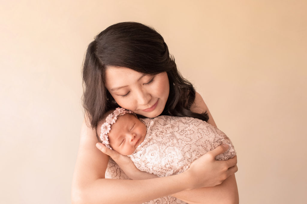 Gainesville newborn portraits beautiful mom Vera holding very close her baby girl wrapped in matching cream fabric with sequins and wearing floral dusty pink crown