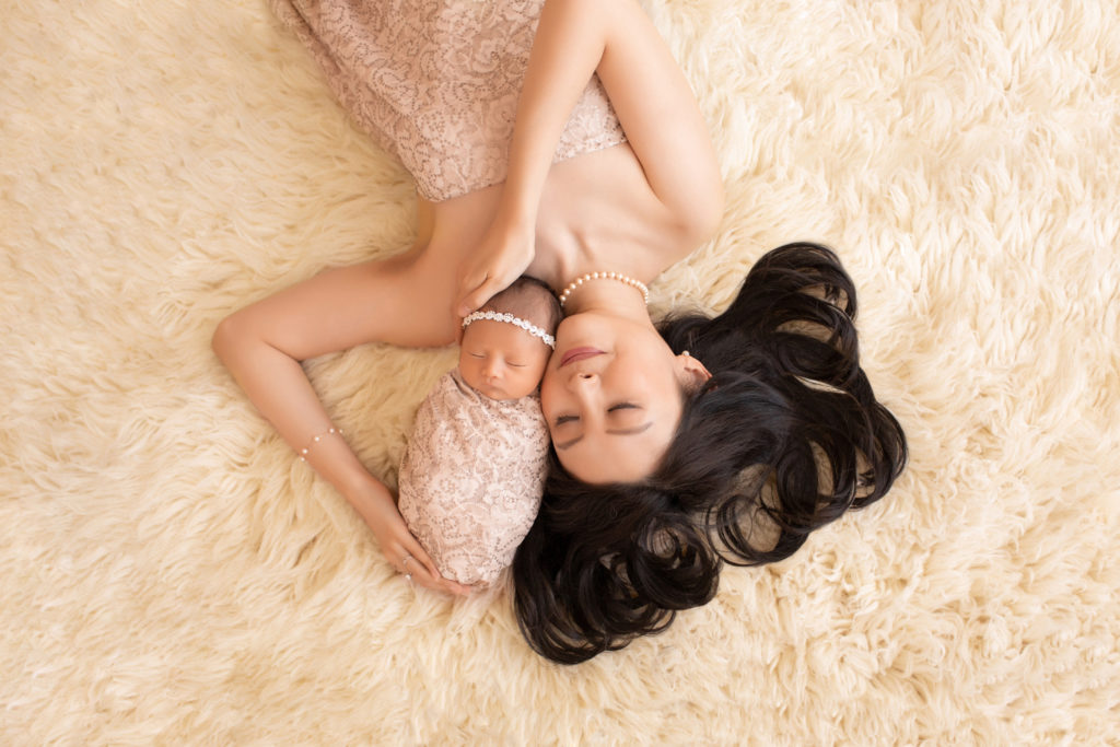 Gainesville newborn portraits beautiful mom Vera with long curly black hair lying on cream fur holding close her baby girl wrapped in matching cream fabric with sequins and wearing pearl head tie to match moms pearl necklace