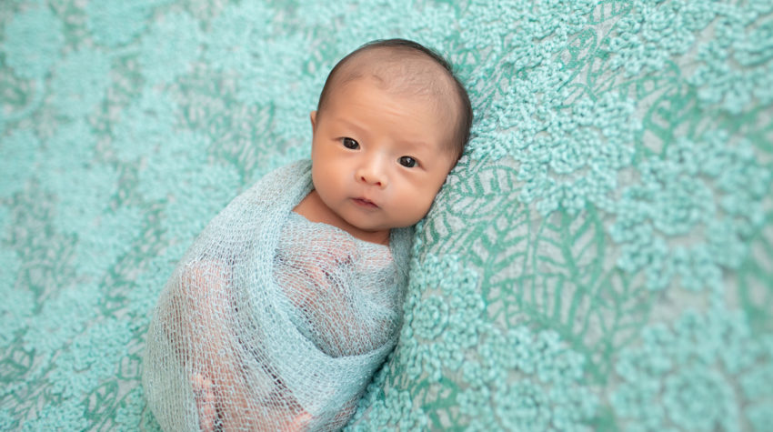 Gainesville newborn portraits baby girl looking straight at camera with her eyes open wrapped in aqua fabric and lying on pale aqua floral blanket