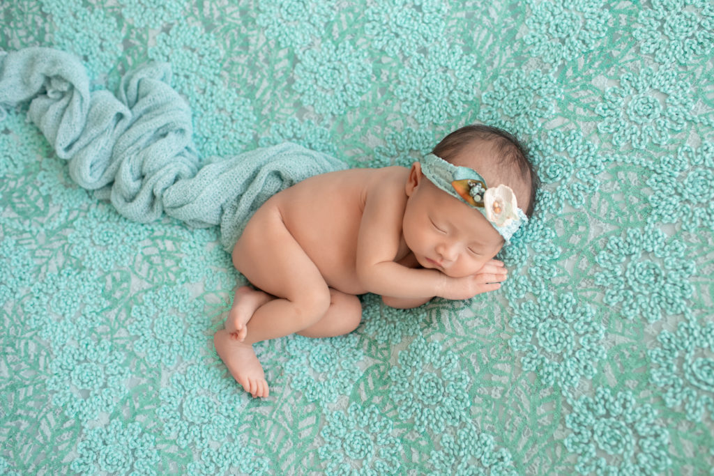 Gainesville newborn portraits naked baby girl soft baby skin with aqua floral head tie lying on pale aqua floral blanket with her side and hand close to face