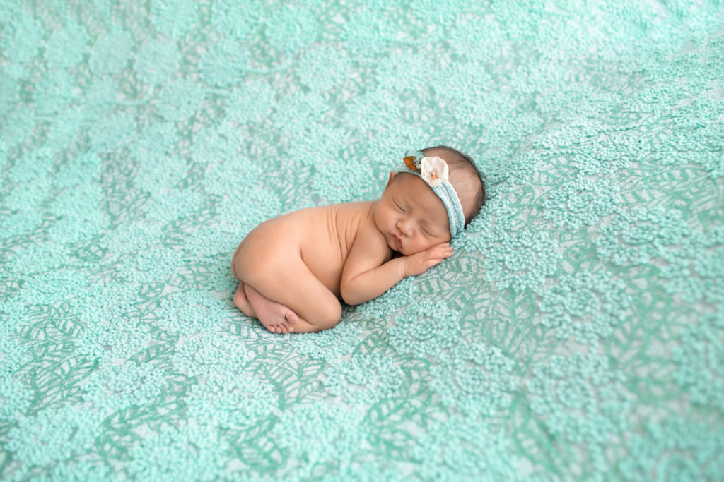 Gainesville newborn portraits naked baby girl soft baby skin with aqua floral head tie posed on pale aqua floral blanket with her bottom up and hand close to face