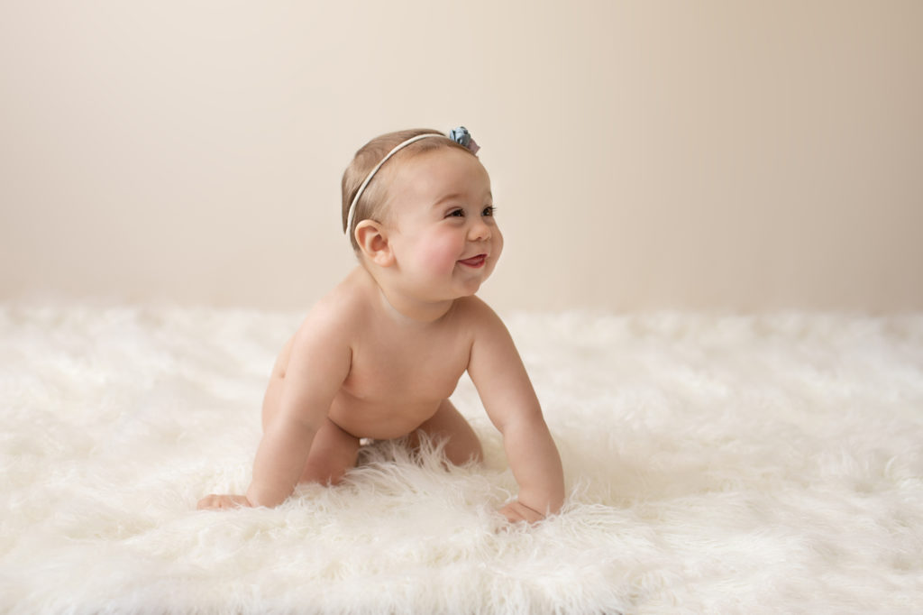 baby photo eight month girl Madison naked soft baby skin pink floral head crawling on white fur with cream backdrop Gainesville Florida