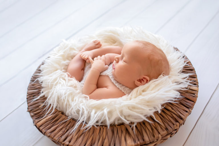 Newborn baby boy Ezra sleeping on white fur in brown basket with backlight Gainesville Florida newborn photographer