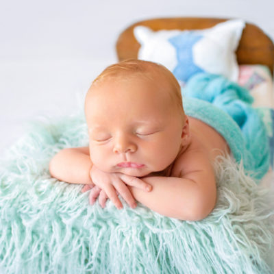 Newborn baby boy Ezra sleeping with his chin on his wrists on quilt covered brown wooden baby bed Gainesville Florida newborn photographer