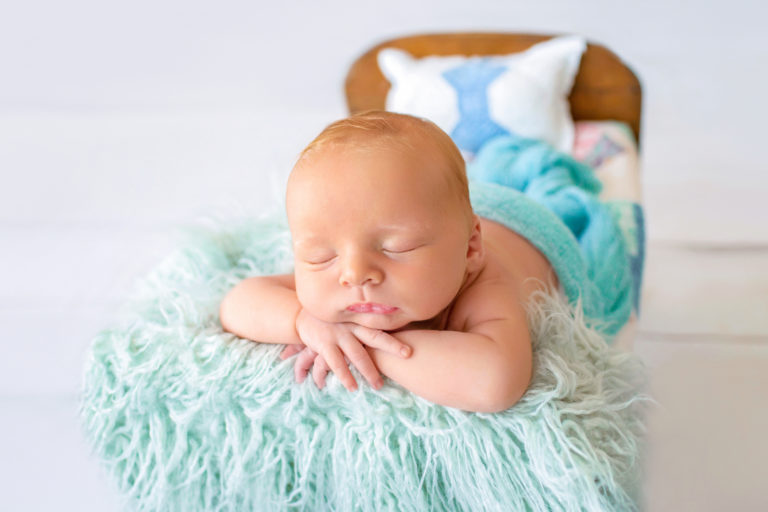 Newborn baby boy Ezra sleeping with his chin on his wrists on quilt covered brown wooden baby bed Gainesville Florida newborn photographer