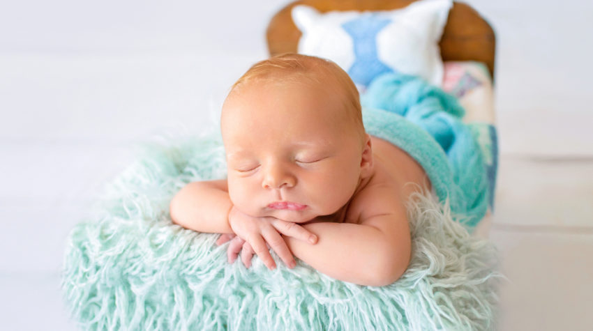 Newborn baby boy Ezra sleeping with his chin on his wrists on quilt covered brown wooden baby bed Gainesville Florida newborn photographer